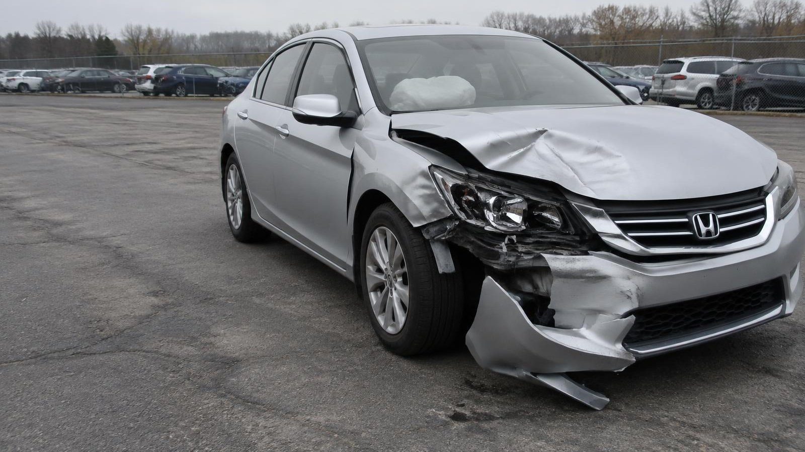 A wrecked silver Honda Accord with severe front-end collision damage in a salvage lot.
